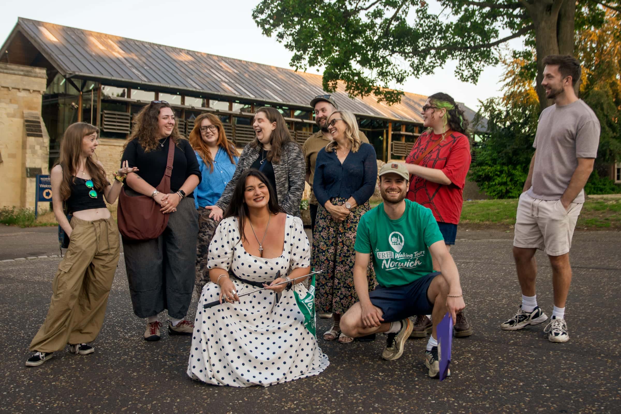 A tour group posing with their guides and the green flag in the grounds of Norwich Cathedral