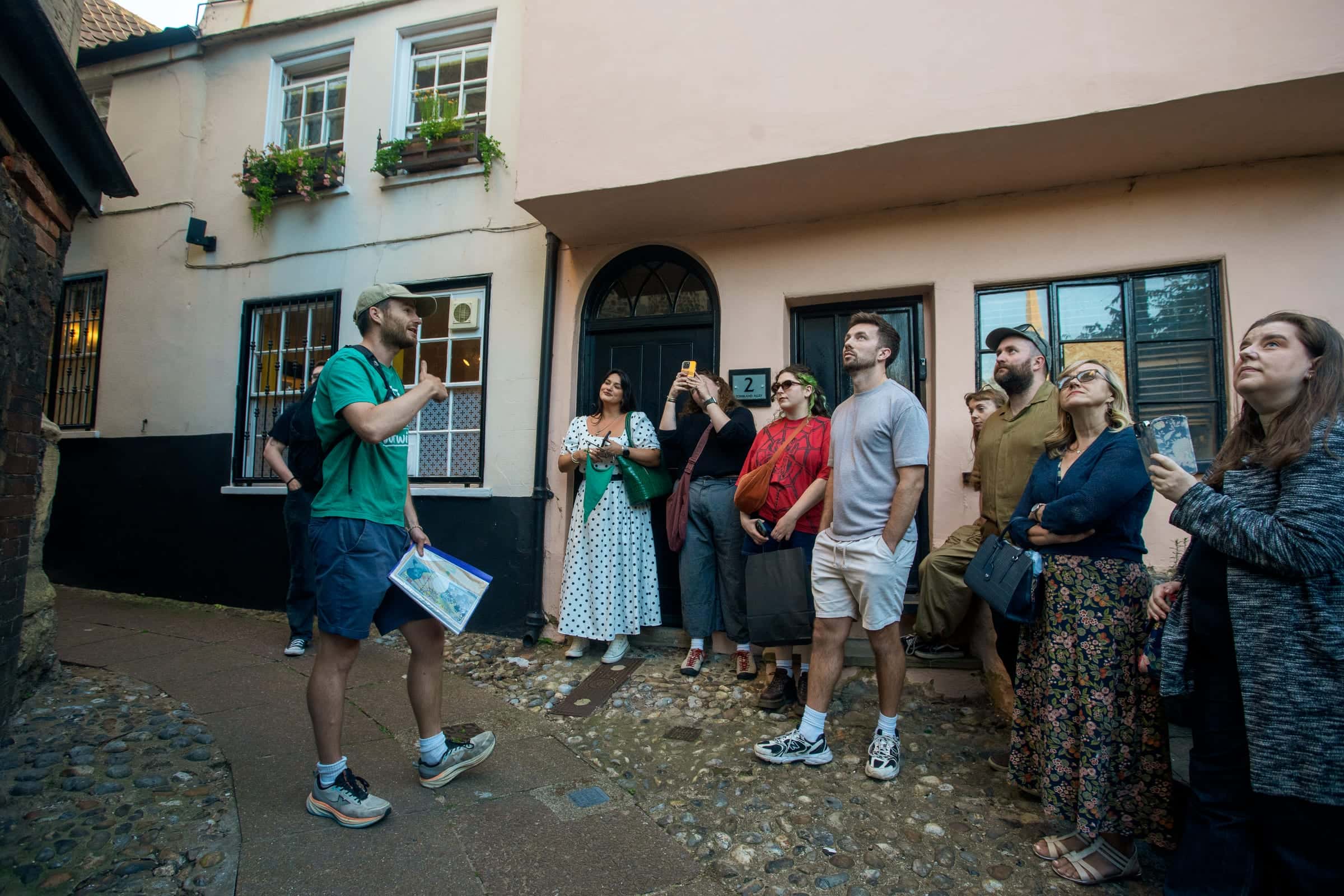 Tom mid-story in Tombland with a tour group listening in front of a pink cottage
