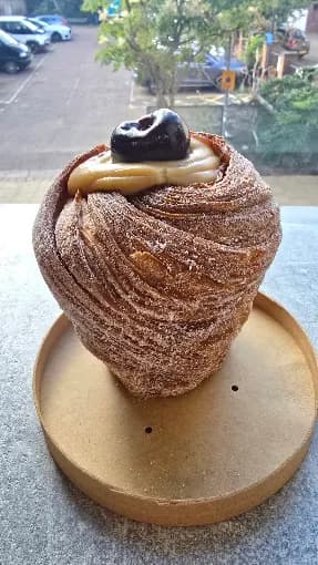A cruffin at DeVecchio Bakery, dusted in sugar and topped with cream and a prune, on a wooden stand in the window.